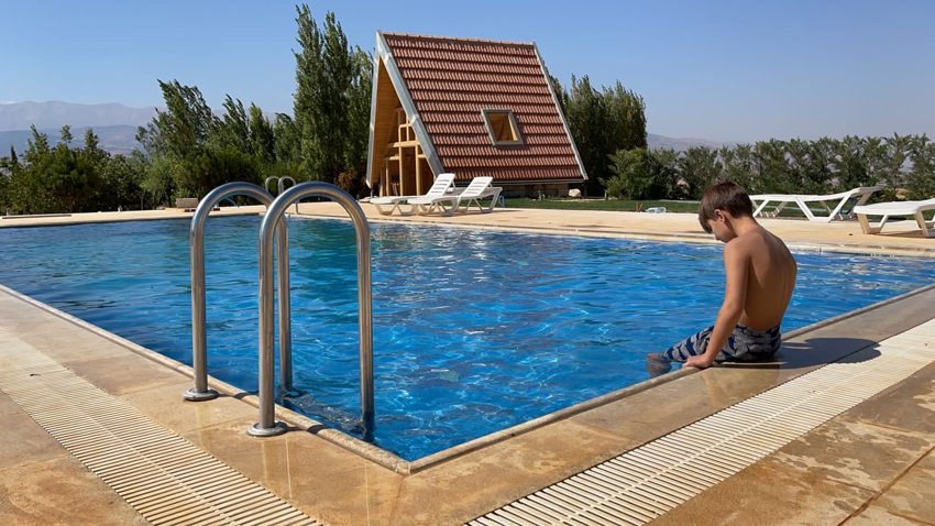 Blue outdoor swimming pool with stainless steel ladder and surrounding terrace